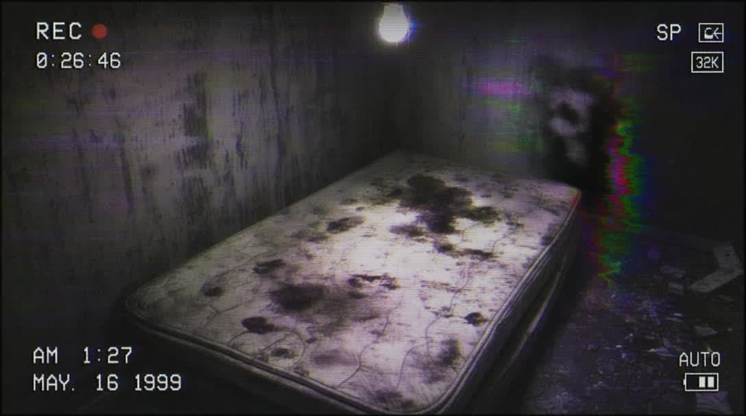 Found footage still: camcorder view of a grimy room and stained mattress